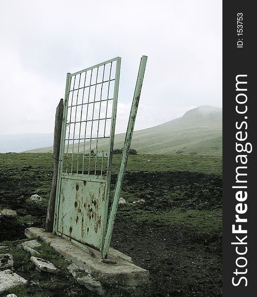 A broken green door standing alone in the middle of a mountain meadow. A broken green door standing alone in the middle of a mountain meadow