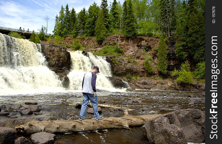 Teen crossing a stream on a log below a waterfall. Teen crossing a stream on a log below a waterfall