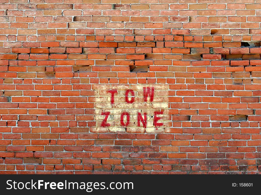 tow zone warning, painted on a crumbling red brick wall