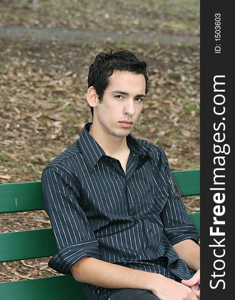 A young man sitting on a park bench looking pensive