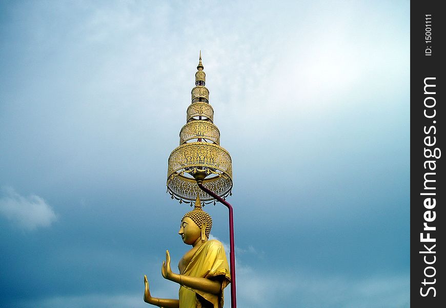 A beautiful stand buddha.Golden tone 
color and Thai art style umbrella.Stand 
buddha located in frint of temple gate. A beautiful stand buddha.Golden tone 
color and Thai art style umbrella.Stand 
buddha located in frint of temple gate