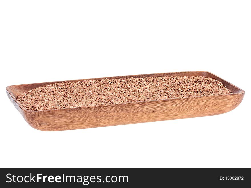 Grains of buckwheat groats in a wooden long plate on a white background.