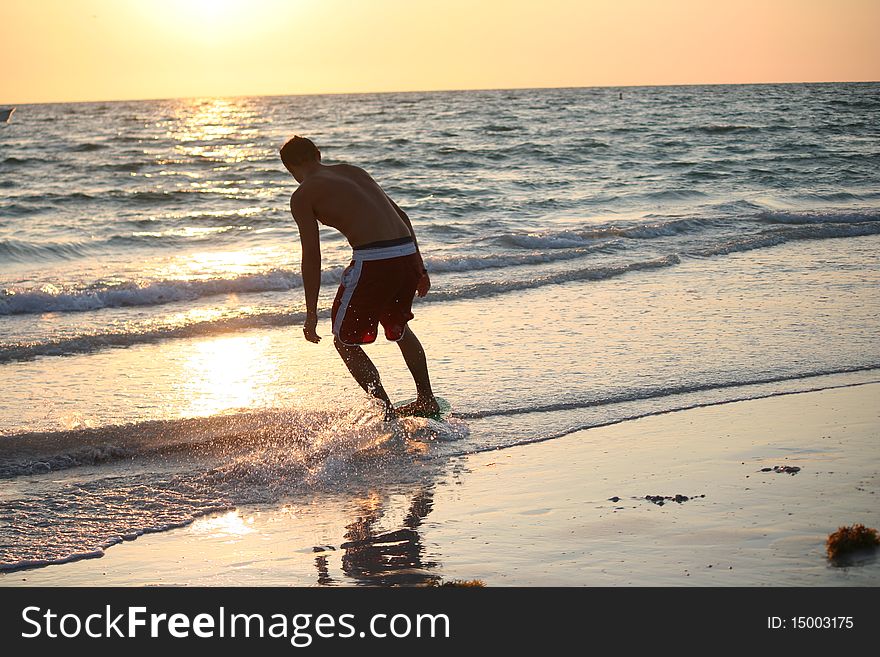 A young man Skim boarding at sunset.