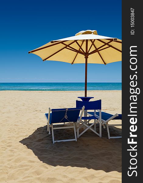 Deck chairs under an umbrella in the sand against the blue sea