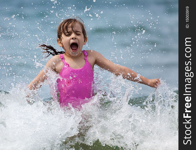 Little girl laughing and crying in the spray of waves at sea on a sunny day