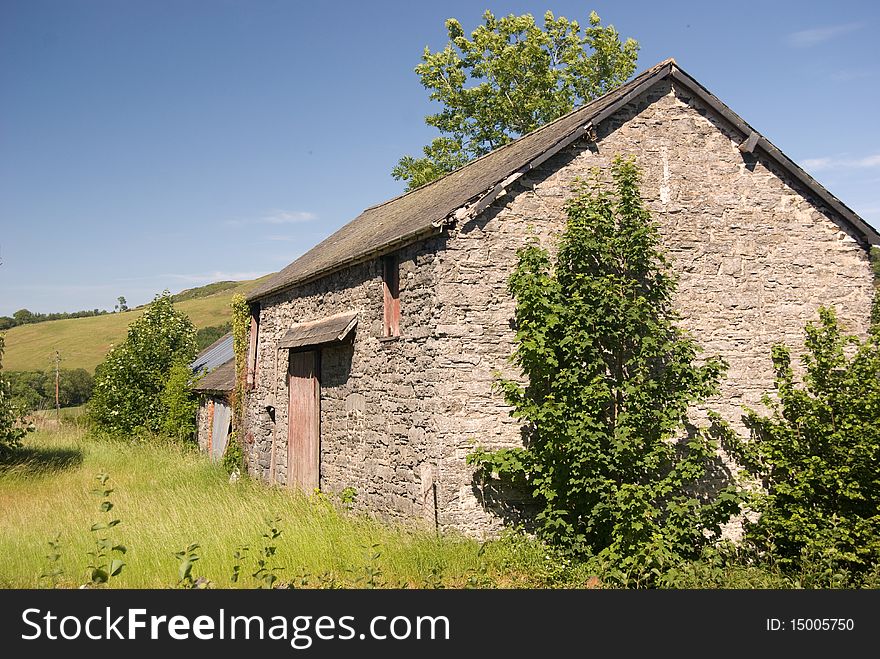 An old stone barn in a sunlit field against blue skies