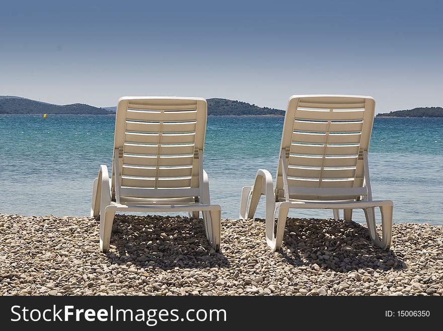 Two beach plastic chairs on the beach in front of blue sea