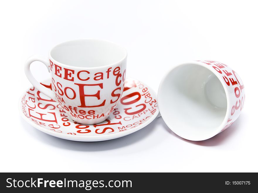 Red and white coffee cups, one of which is on the saucer, the other upside down, on a white background