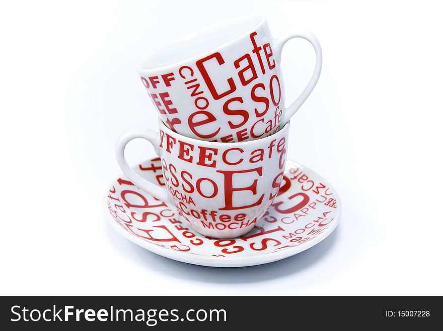 Two are white with a red patterned coffee cups, facing one another on a saucer on a white background. Two are white with a red patterned coffee cups, facing one another on a saucer on a white background