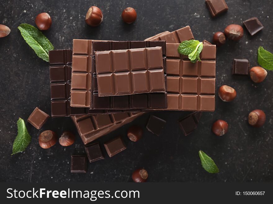 Flat lay composition with tasty chocolate, mint and hazelnuts on dark background