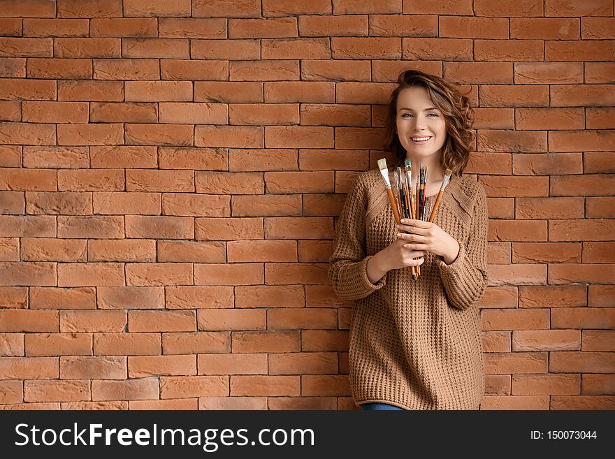 Female artist with brushes on brick wall background