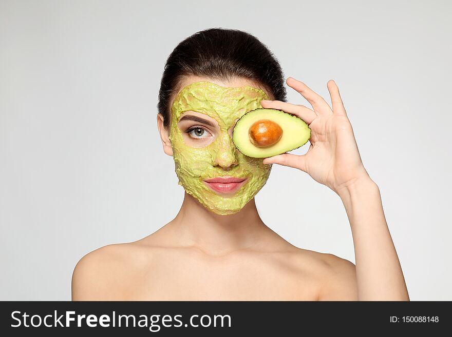 Beautiful Young Woman With Facial Mask And Fresh Avocado On Light Background