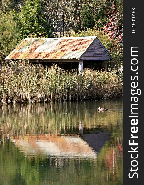 A rustic old shed in a rural area reflects in the afternoon sunlight onto a lake. A rustic old shed in a rural area reflects in the afternoon sunlight onto a lake.