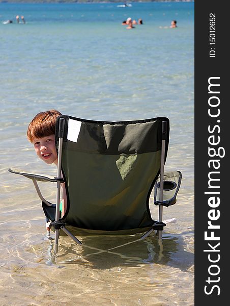 A smiling young boy cooling off by sitting in a chair that is in the lake. Taken at Crystal Lake in Beulah, Michigan. A smiling young boy cooling off by sitting in a chair that is in the lake. Taken at Crystal Lake in Beulah, Michigan.