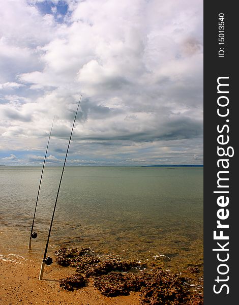 2 fishing rods wait on the beach for a catch. Beautiful summery beach scene. Relaxing!. 2 fishing rods wait on the beach for a catch. Beautiful summery beach scene. Relaxing!