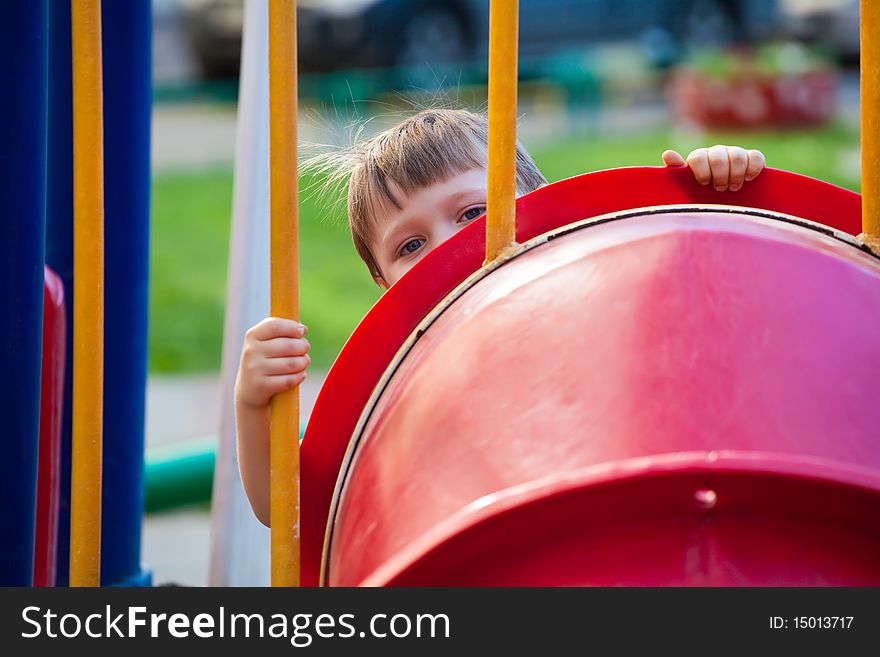 Child looks out of an attraction pipe in park. Child looks out of an attraction pipe in park