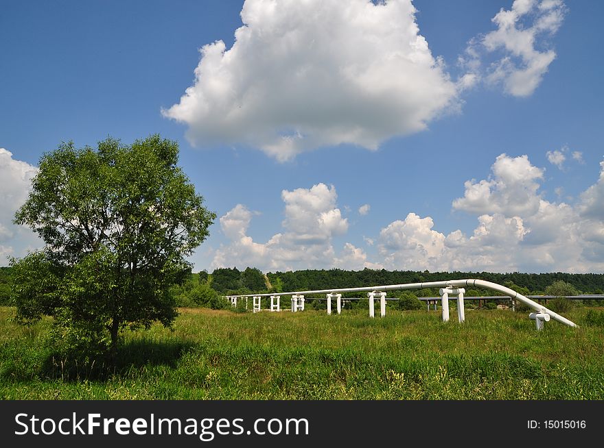 The main oil pipeline of a high pressure in a summer landscape under clouds. The main oil pipeline of a high pressure in a summer landscape under clouds.