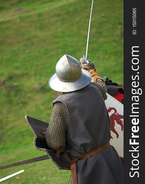 Medieval knight with metal helmet and sword running towars enemy in battlefield. The armored man in the photo is photographed from behind. Medieval knight with metal helmet and sword running towars enemy in battlefield. The armored man in the photo is photographed from behind.