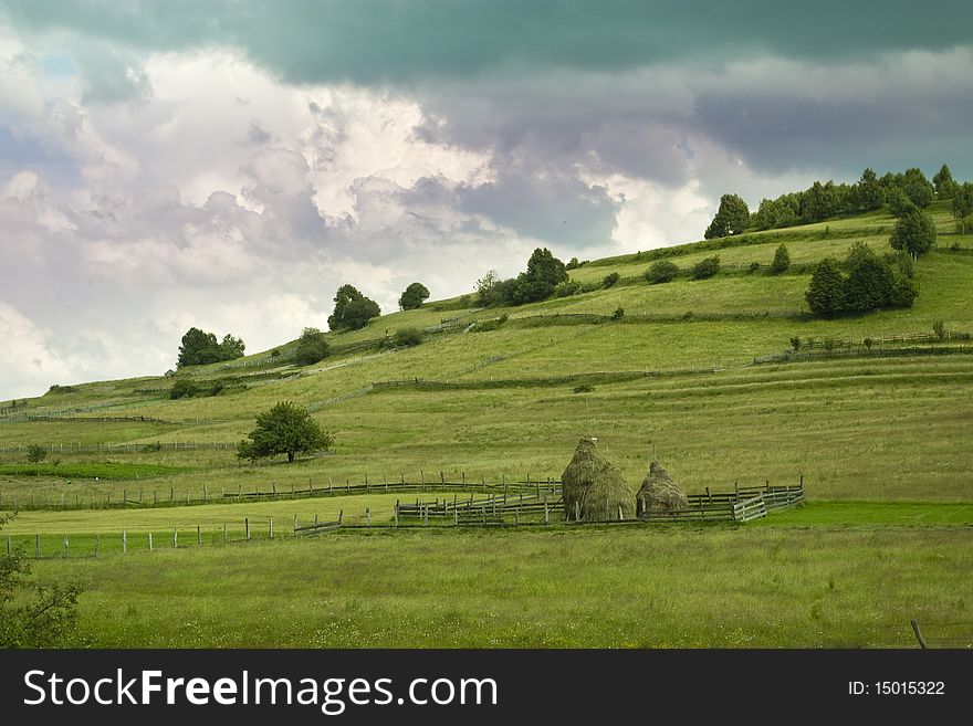 Mountain pasture landscape with haystacks, spectacular cloudscape in Transylvania, Romania