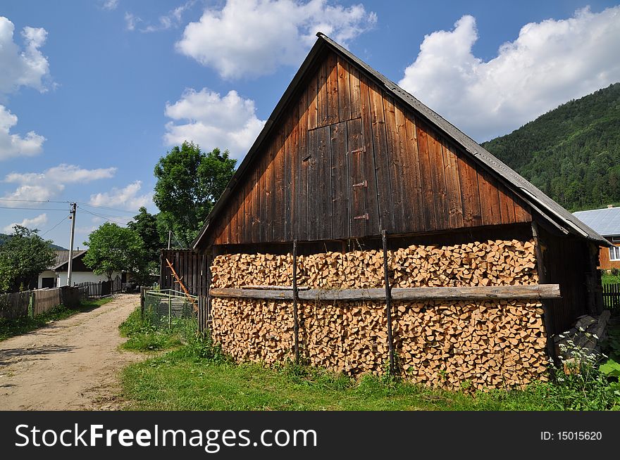 An end face of a wooden shed with accurately laid fire wood in a rural landscape. An end face of a wooden shed with accurately laid fire wood in a rural landscape