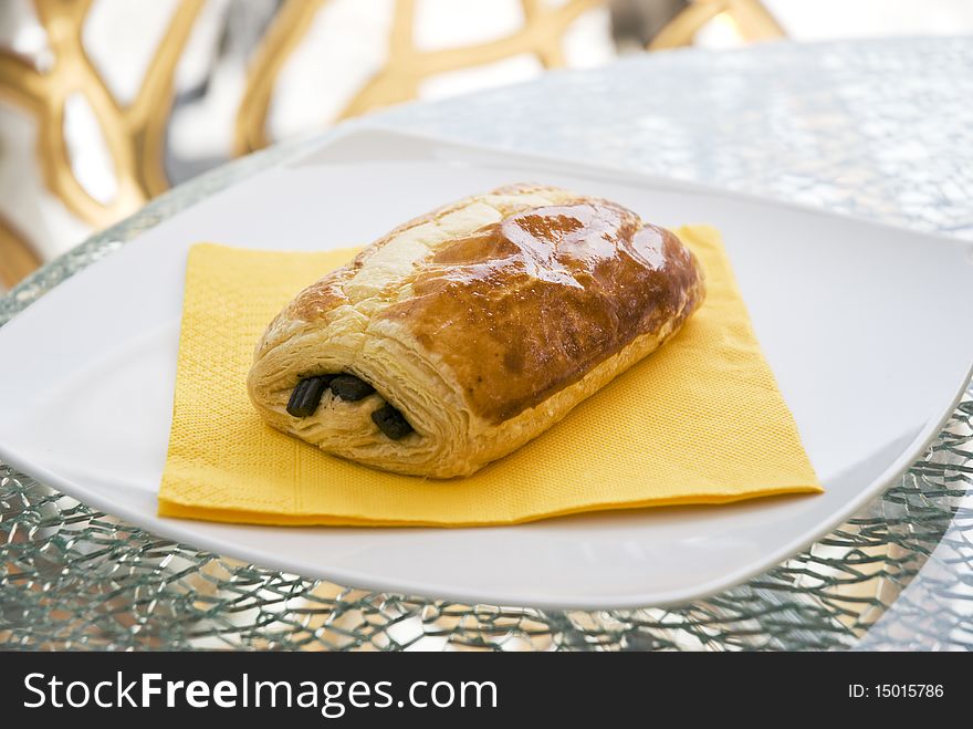 A color photo of a freshly baked chocolate croissant on a yellow napkin and white plate.