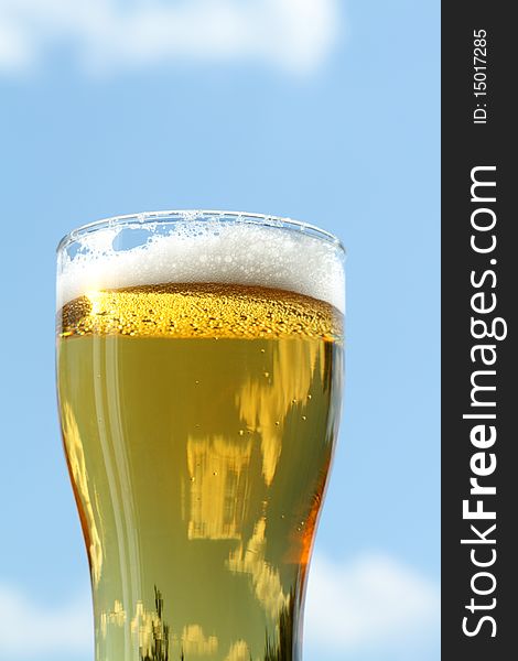 Closeup of beer glass with foam on blue sky background