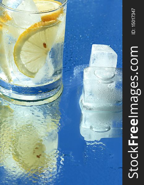Glass of water with lemon and ice cubes on blue background. Glass of water with lemon and ice cubes on blue background