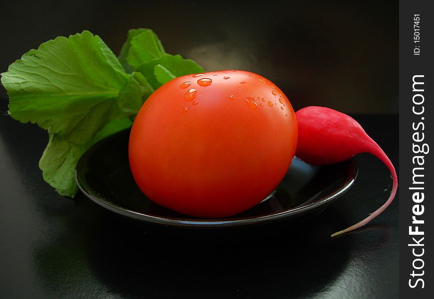 The vegatables - the red tomato with radish on a black plate