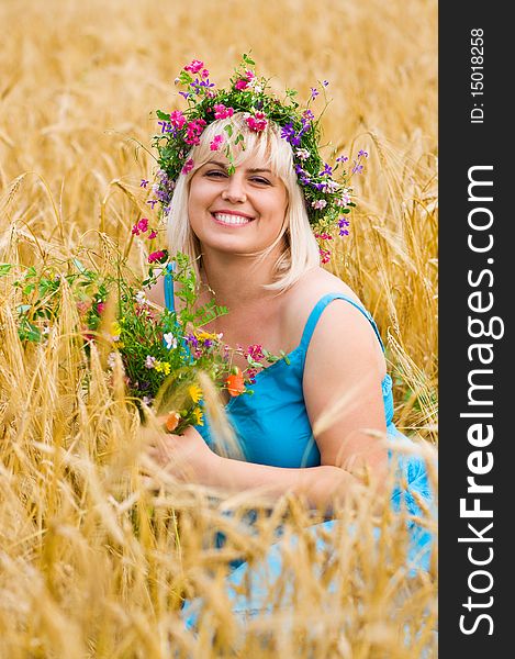 Beautiful woman in wreath of wild flowers in wheat meadow on sunny day. Beautiful woman in wreath of wild flowers in wheat meadow on sunny day