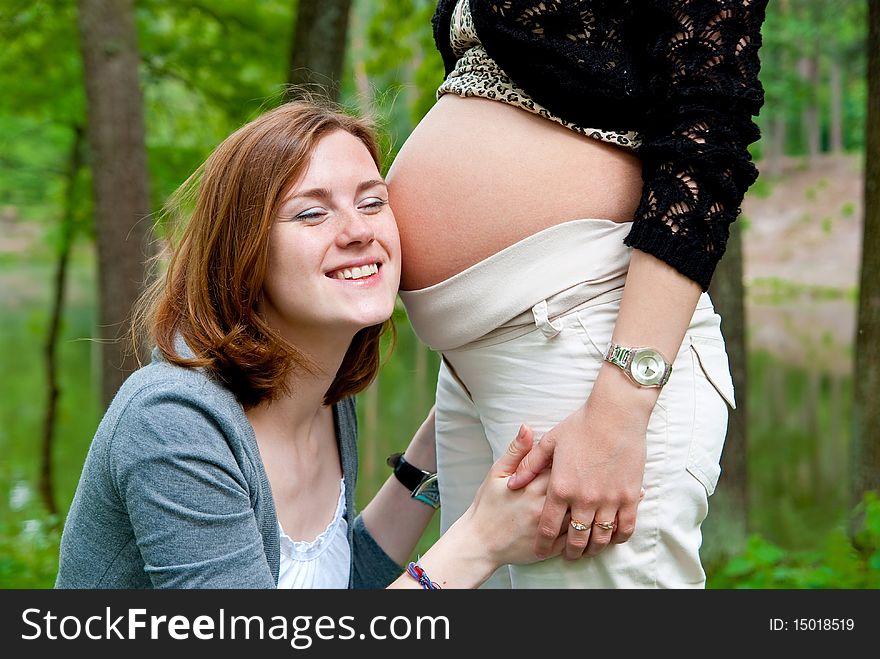 Girl listening pregnant belly. Outdoor shot