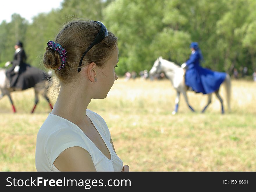 Girl watching a horsewoman ride in blur. Girl watching a horsewoman ride in blur