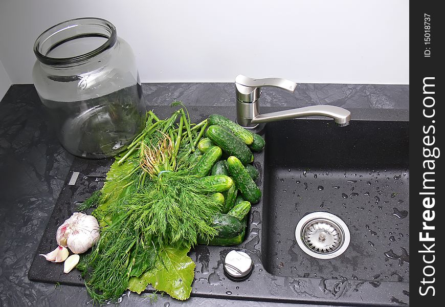 The big jar on the black sink with washed cucumbers and other ingredients ready to cucumbers pickling.