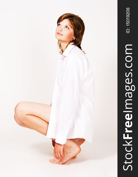 Pretty young woman in a white shirt sitting on gray background