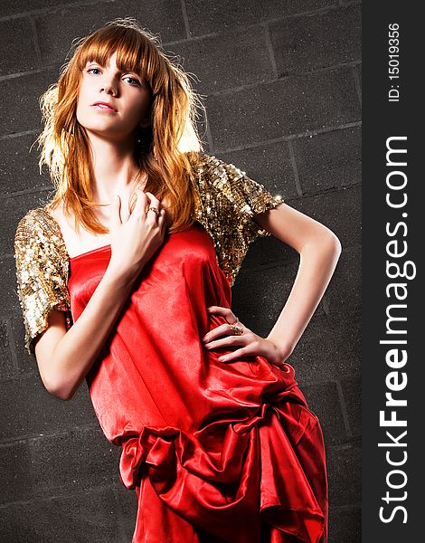 Fashionable red-haired woman in a satin red dress against brick wall background