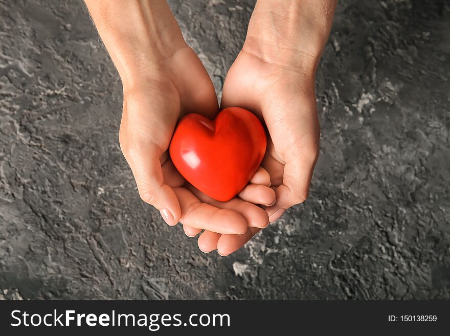 Hands of woman with red heart on dark textured background