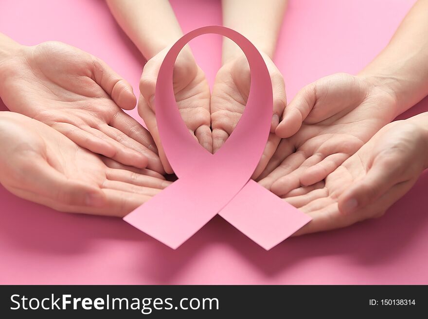 Female hands holding pink ribbon on color background. Breast cancer awareness concept