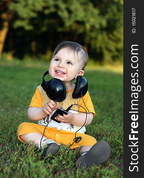 Little boy with headphones sitting on the grass. He was smiling from ear to ear. Little boy with headphones sitting on the grass. He was smiling from ear to ear