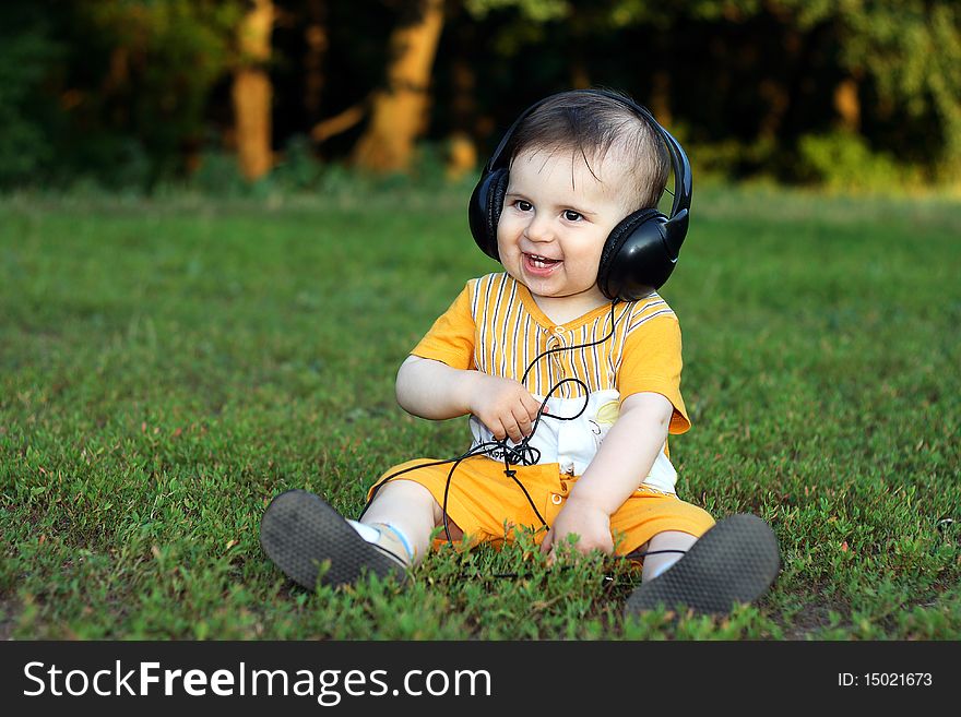 Little boy with headphones sitting on the grass. He is smiling and he is very happy. Little boy with headphones sitting on the grass. He is smiling and he is very happy