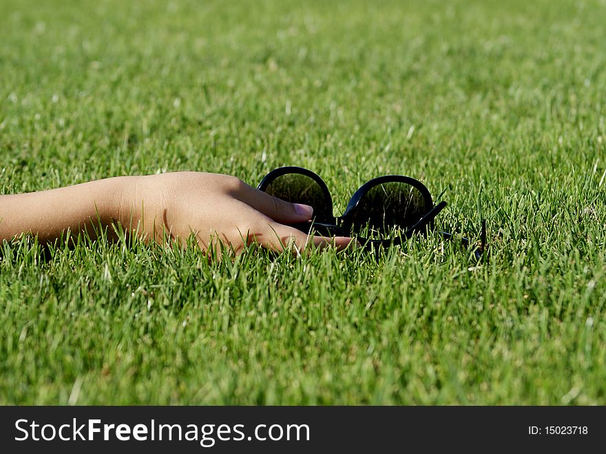 A woman's hand holding a pair of sunglasses on green grass. A woman's hand holding a pair of sunglasses on green grass