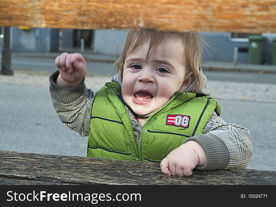 Angry little child behind the bench threatens. Angry little child behind the bench threatens