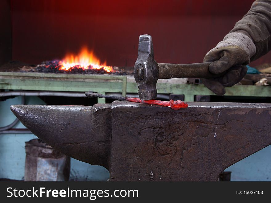 The hand of the smith strikes a hammer on the heated metal on an anvil against fire