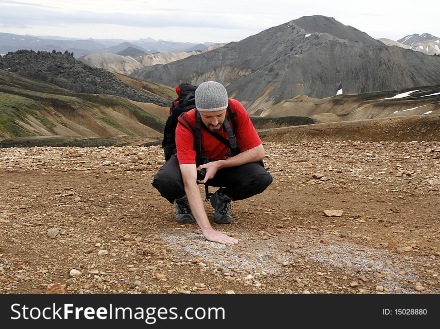 Young male traveller touching warm sulfur ground of geothermal Landmannalaugar region in iceland