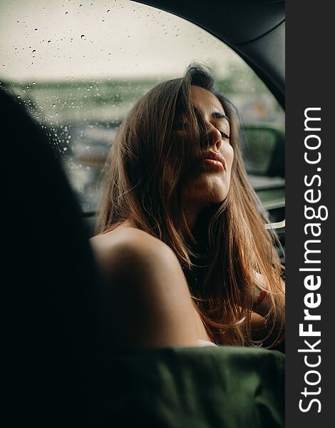 A young woman sits inside a car against the background of raindrops