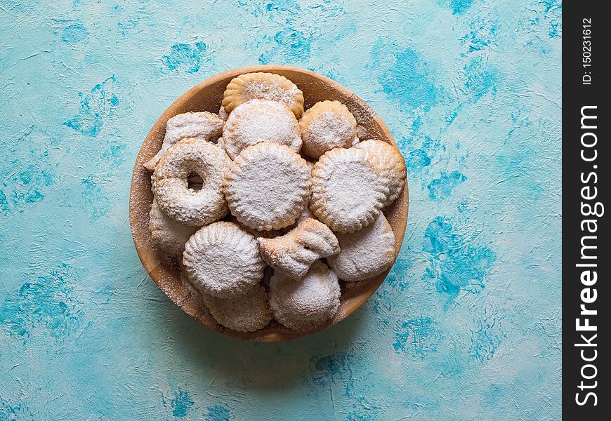 Holiday cookies sprinkled with powder in a wooden bowl on a blue background. Holiday cookies sprinkled with powder in a wooden bowl on a blue background.