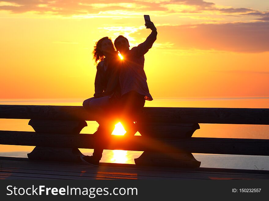 Silhouette young couple at sunset by the sea. Selfie