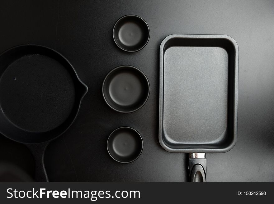 Different sizes black cook pan and black different sizes bowl on black table top. View from above