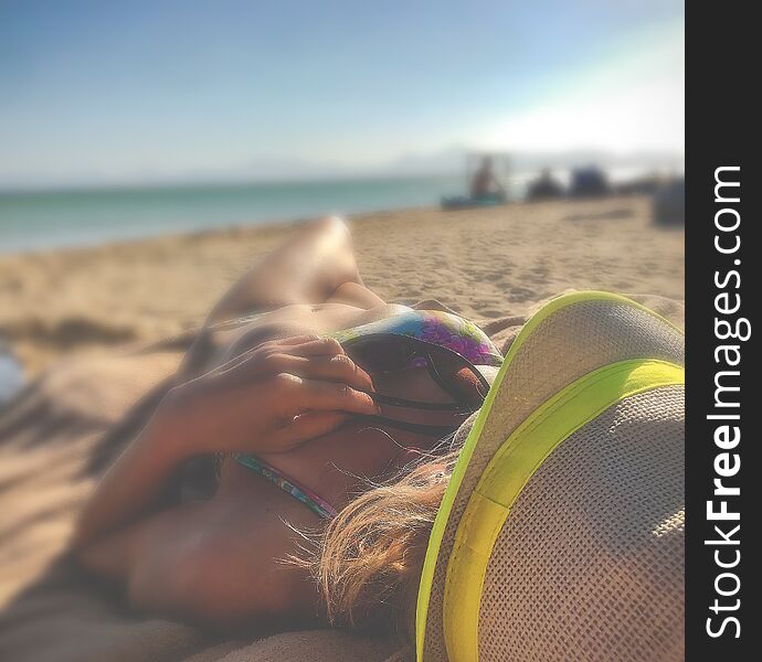 Beautiful tanned figure young girl lies on the beach in yellow hat from overheating sun