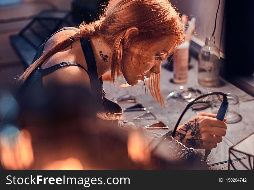 Beautiful diligent woman is doing soldering at her own artisan lamp studio. Beautiful diligent woman is doing soldering at her own artisan lamp studio.