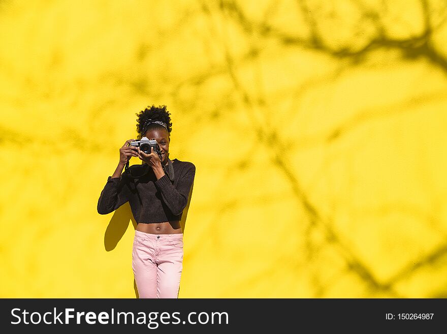 Young african woman in black sweater and pink jeans standing and holding camera outdoor. Young african woman in black sweater and pink jeans standing and holding camera outdoor