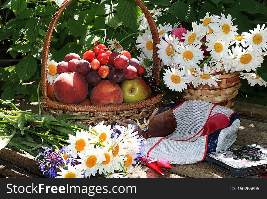 Juicy black grapes and apples, pears and peaches in a basket in the garden on an old wooden table, glasses and a cap, a smartphone surrounded by spring flowers with drops close-up, selective focus. Gathering in the country tasty, dietary and healthy food for a healthy lifestyle